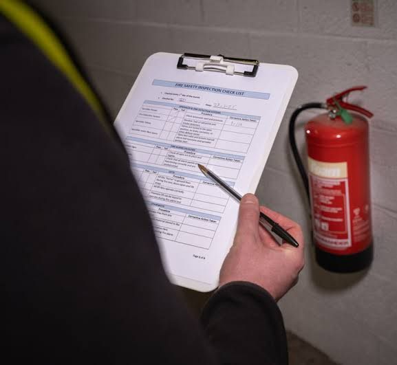 Assessor completing a fire safety inspection checklist beside a red fire extinguisher