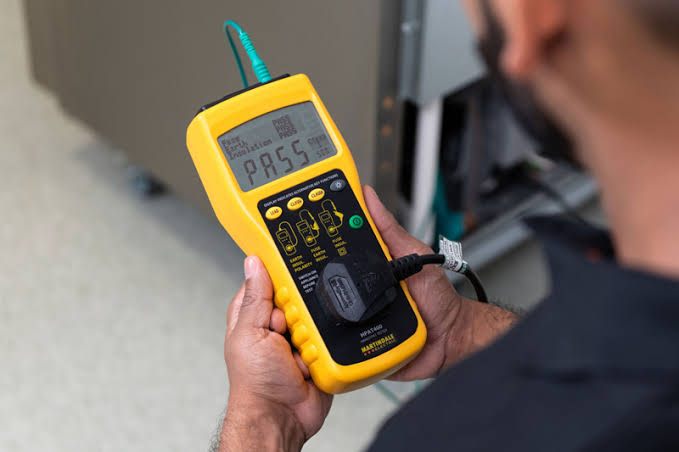 Engineer holding a portable appliance tester displaying a PASS result