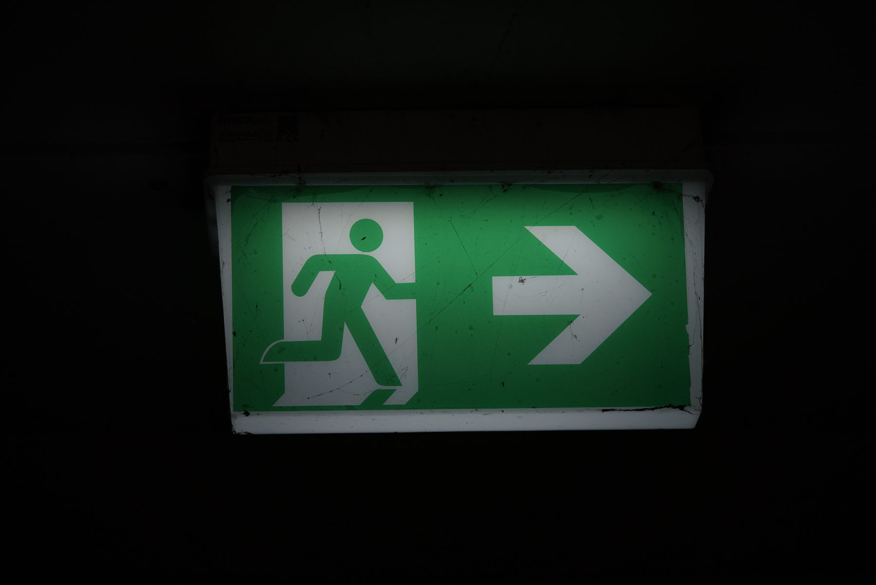 Illuminated green emergency exit sign showing a running figure and directional arrow in a darkened corridor